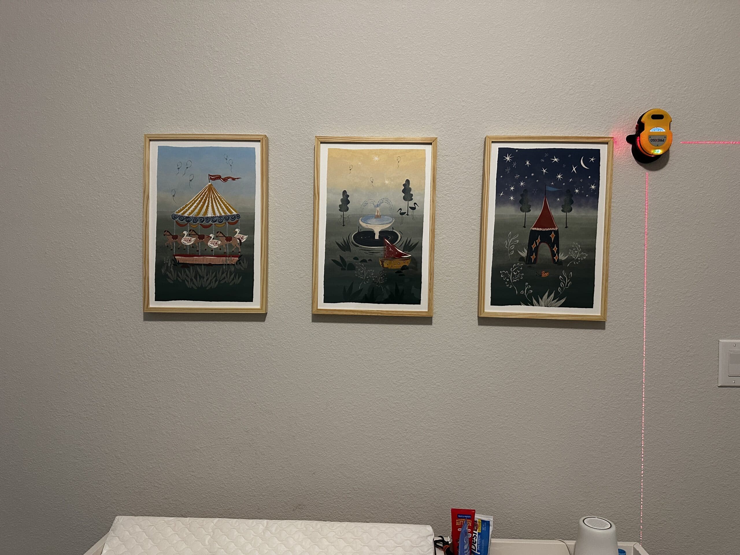 Three framed nursery prints hung in a level row, lined up with a laser level
