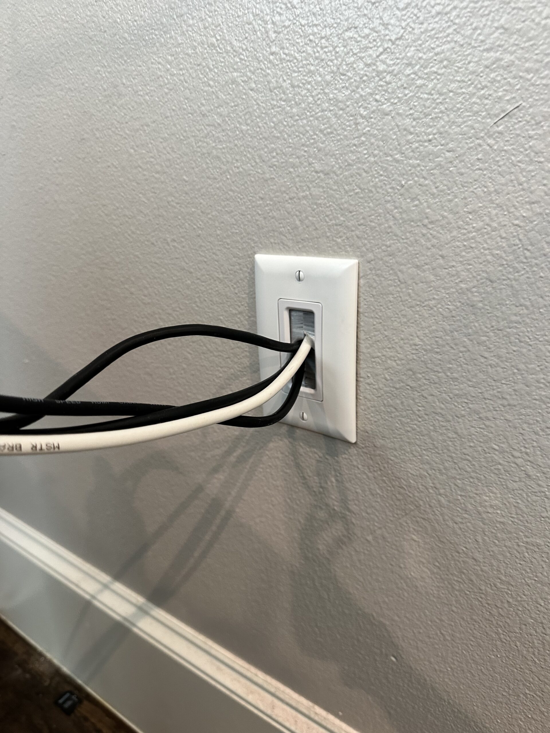 TV cables routed through an in-wall cable pass-through plate to hide wires behind a mounted TV
