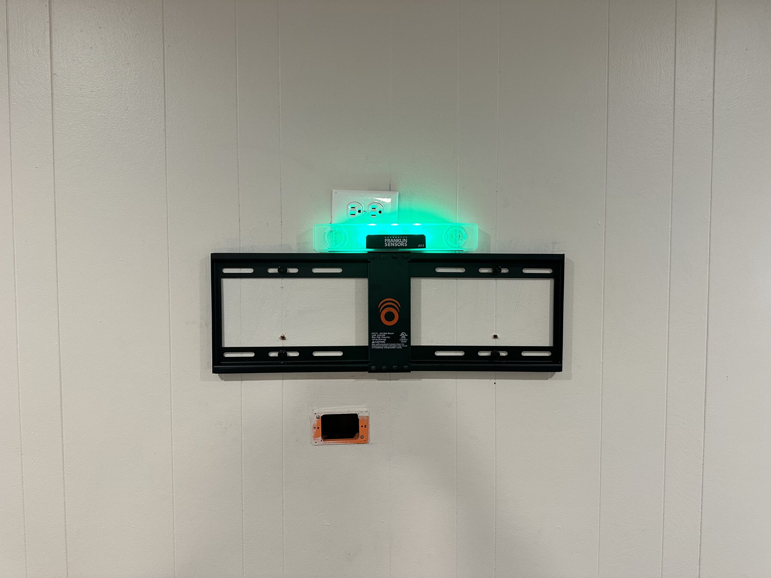 Low-profile TV wall mount being leveled on a paneled wall above a recessed outlet in Dallas