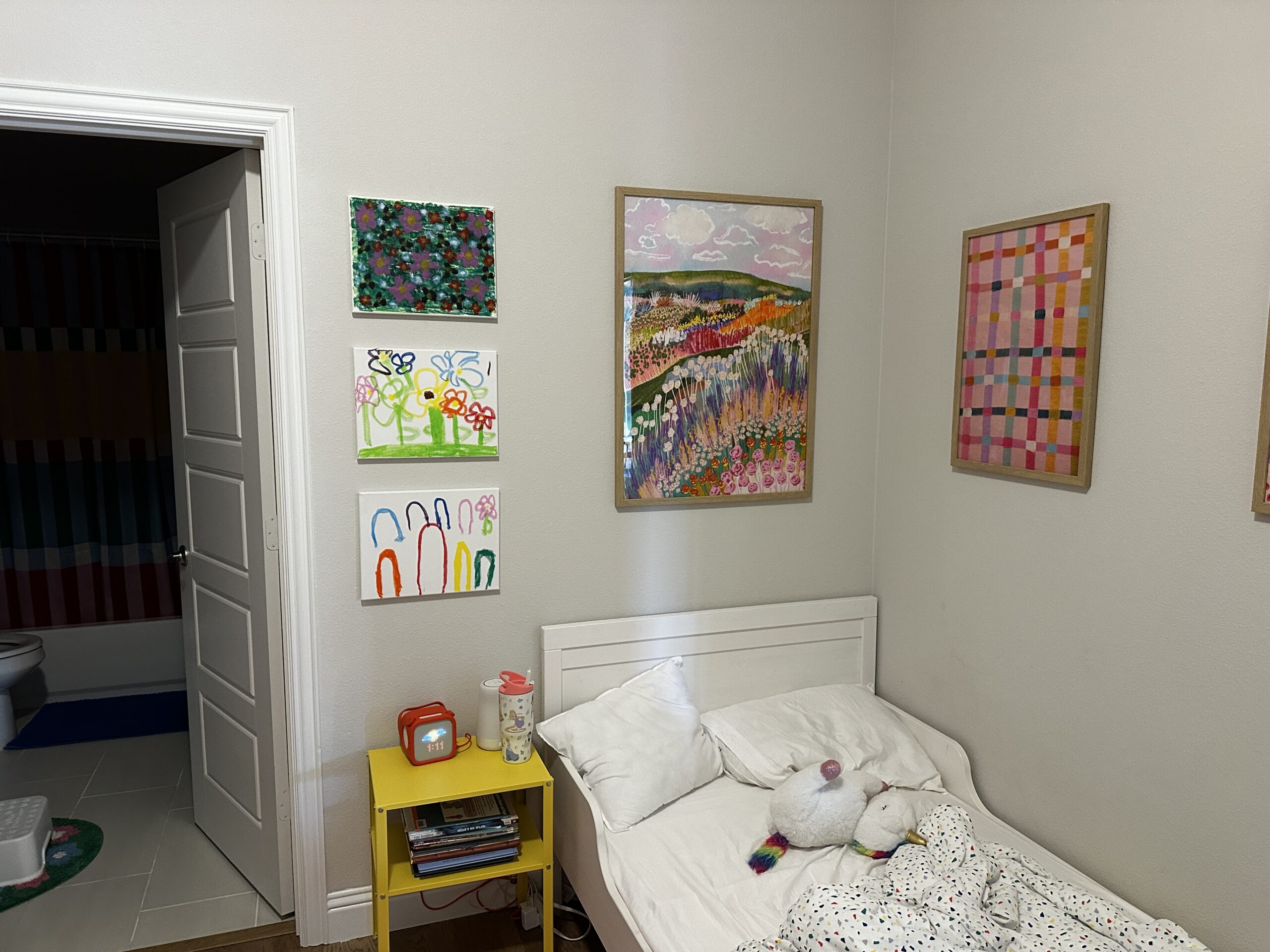 Children's canvases and framed prints hung as a grouping across two walls of a kid's bedroom