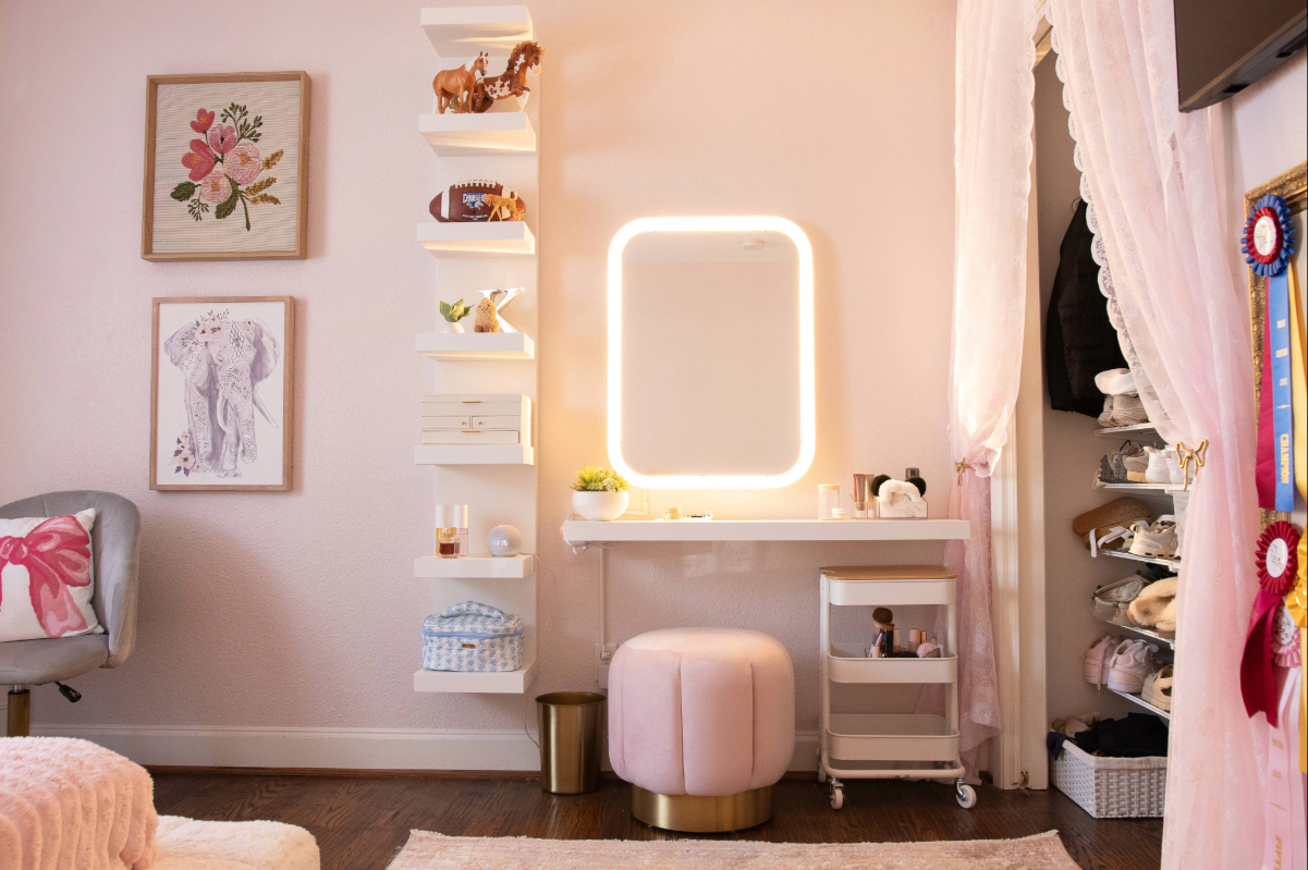 Finished girls' bedroom in Lakewood with a tall white wall shelf unit, a floating makeup desk with a lighted mirror, and a closet curtain held by a brass bow tieback