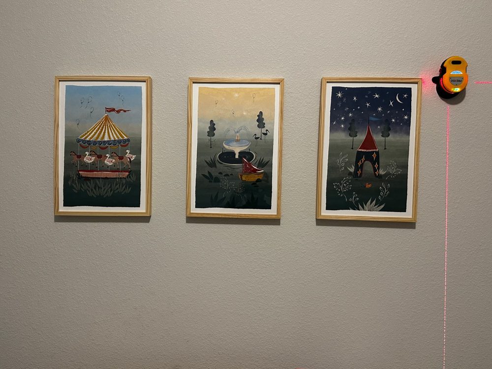 Three framed prints hung level with a laser line in a Dallas nursery