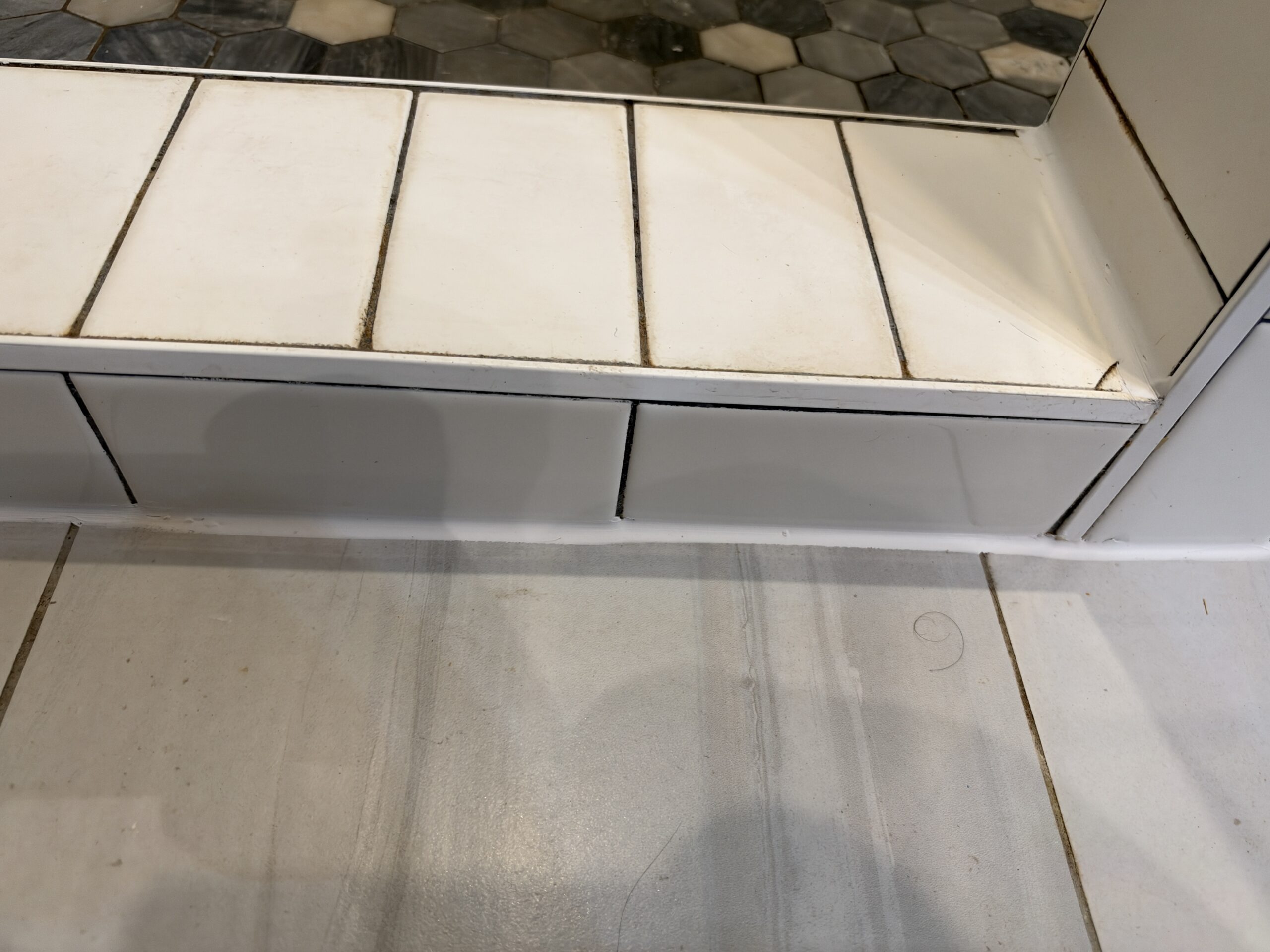 Shower curb and the joint along its base sealed with white silicone caulk in a Sparkman Club bathroom, Dallas
