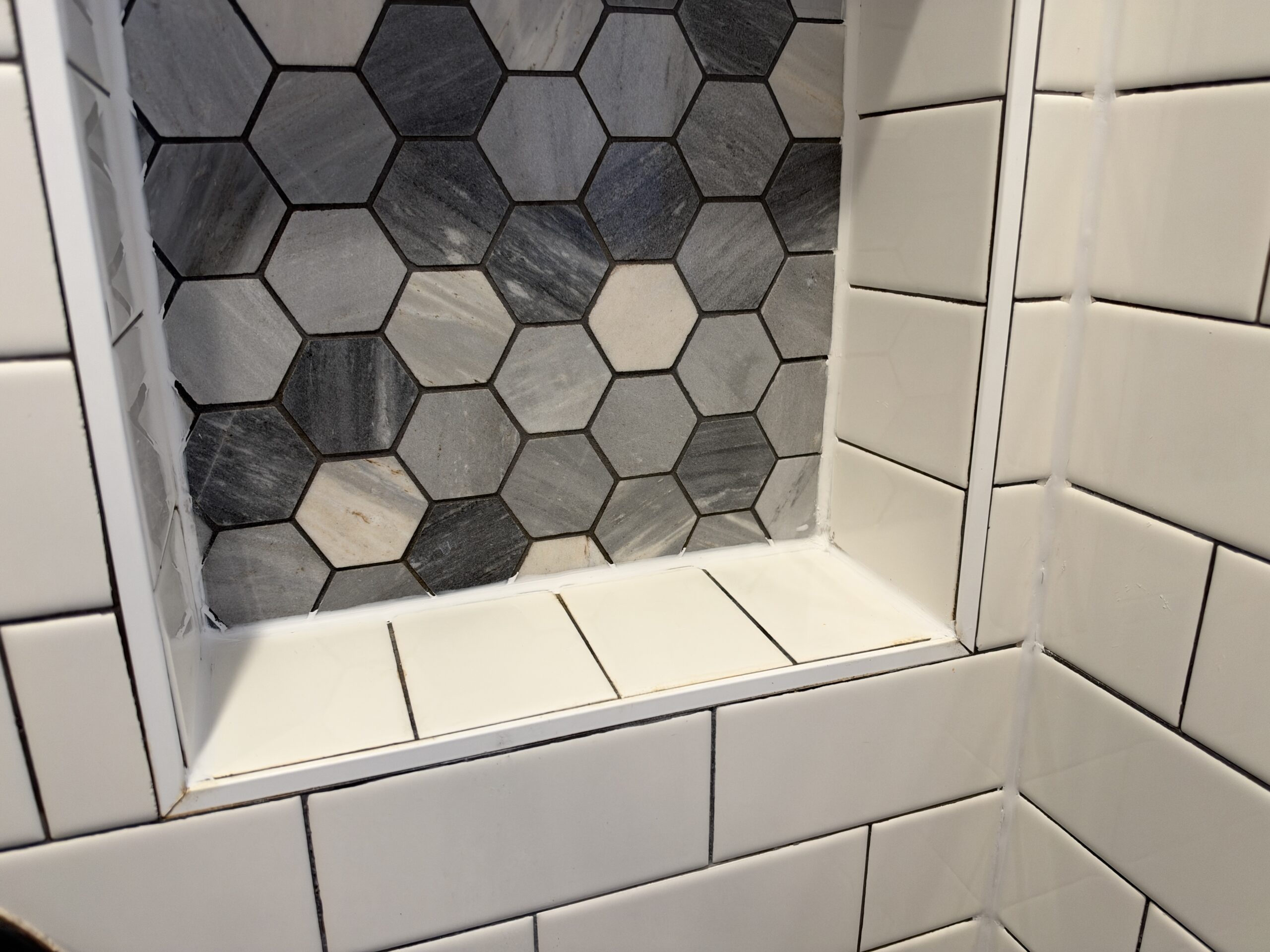 Tiled shower niche in Sparkman Club, Dallas, with its corners sealed in white silicone caulk